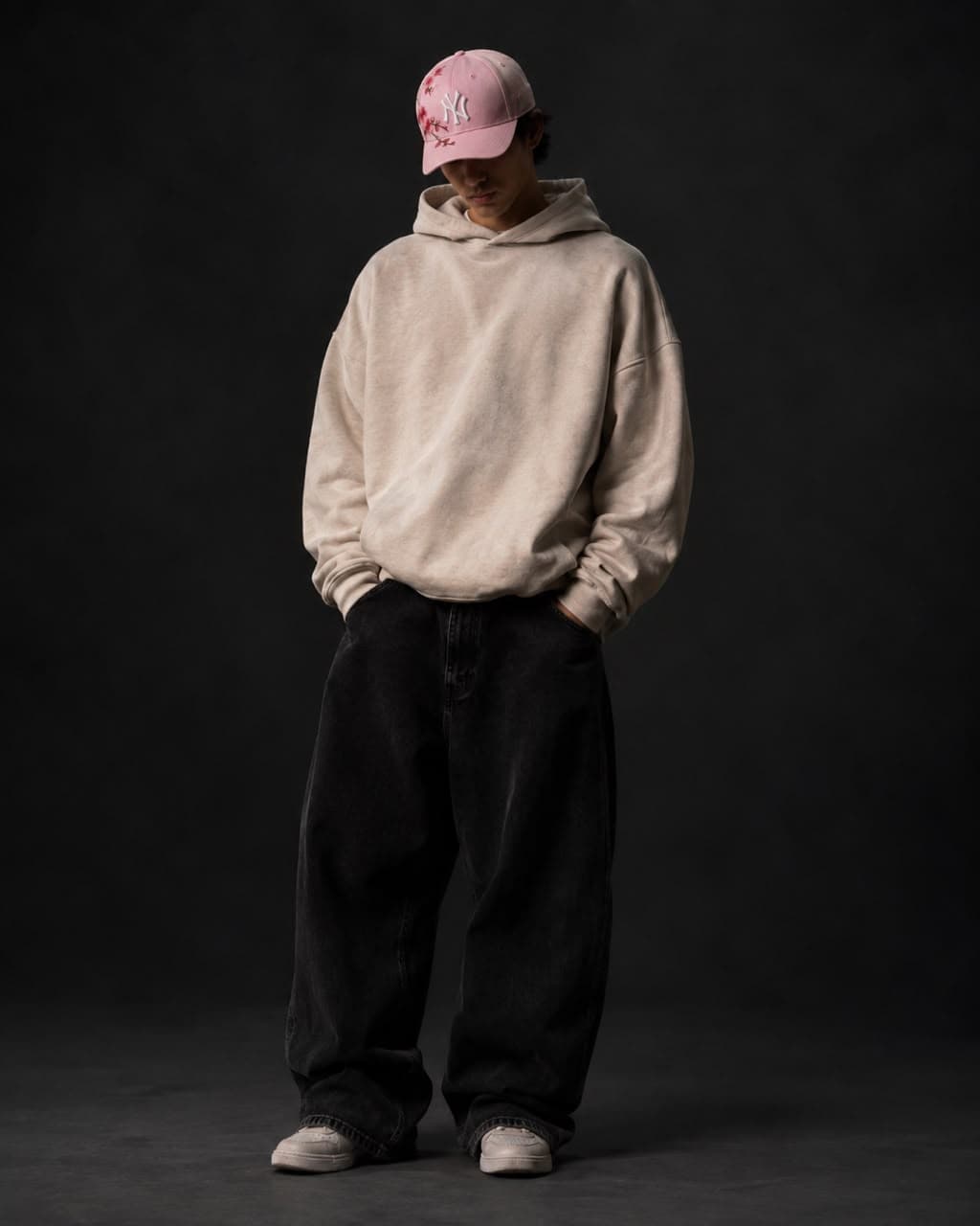 Model wearing the Cherry Bloom cap, pale pink with cherry blossom embroidery, with a cream hoodie