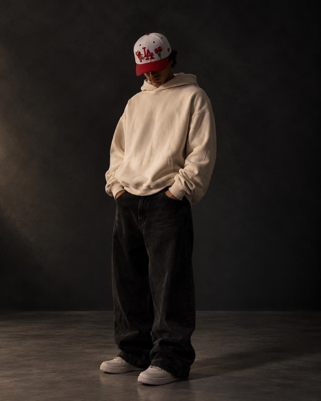 Model wearing the Red District cap, white crown with red floral embroidery, with a cream hoodie